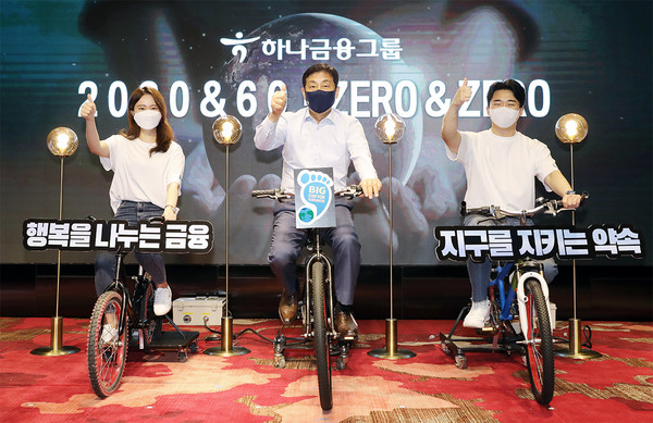 김정태 하나금융그룹 회장(사진 가운데)이 지난 4월 서울 마포구 홍익대학교 인근 'H-PULSE'에서 열린 그룹의 '2030 & 60'·'ZERO & ZERO' 선언 행사에서 하나 핫튜버와 함께 친환경 자가발전 자전거 세리머니를 하고 있다. 사진=하나금융그룹