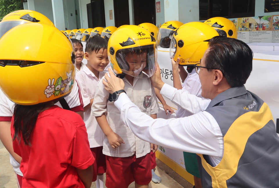 조정래 KB손해보험 인니법인장이 지난 16일 인도네시아 남부 지역 학교 학생들에게 안전모를 씌워주고 있다. 사진=KB손해보험
