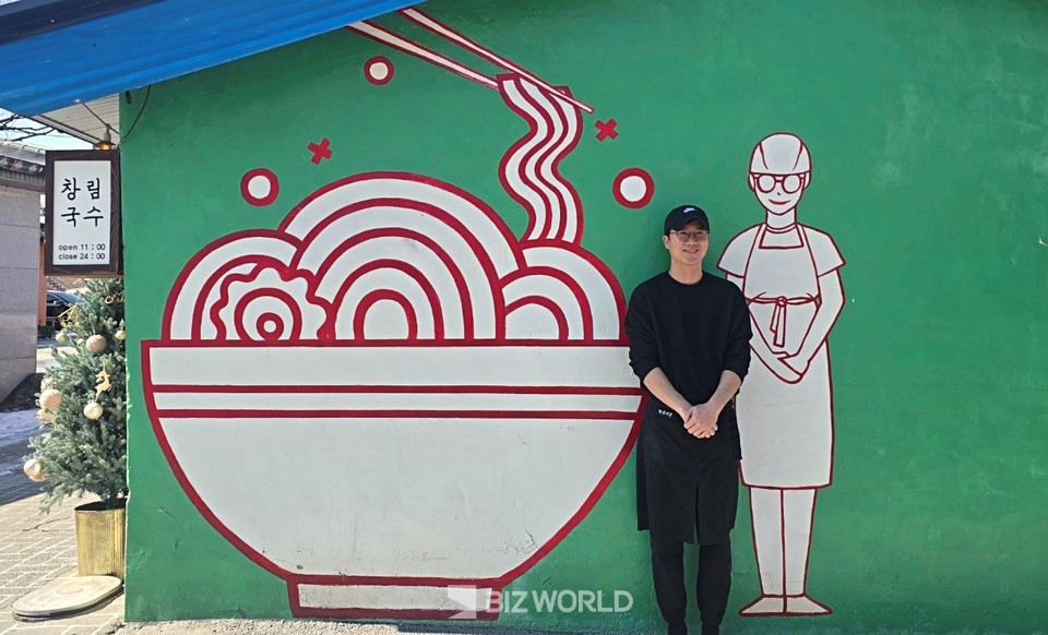 권주철 '창림국수' 사장이 가게를 벽화 앞에서 벽화와 같은 포즈를 취하고 있다. 사진=손진석 기자