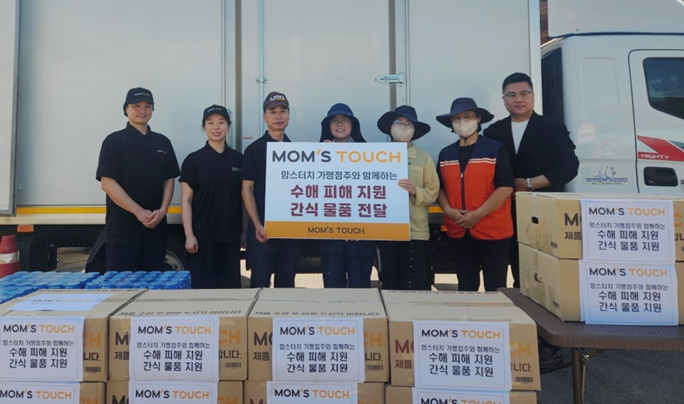 지난 8일 경남 산청군 신안면에 위치한 집중호우 피해 현장에서 맘스터치 본사 임직원 및 가맹점주들이 간식 물품을 전달하고 수해복구 현장 관계자들과 기념촬영을 진행하고 있다. 사진=맘스터치