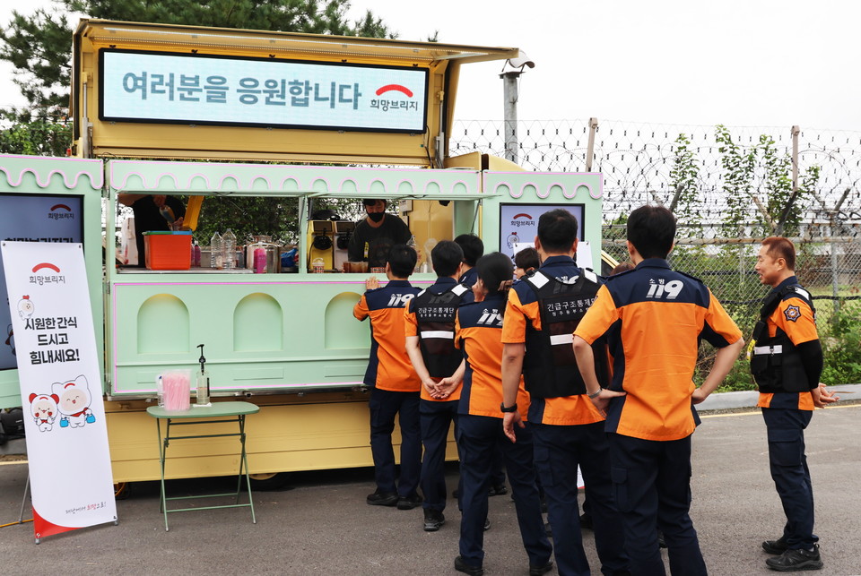 소방대원들이 청주국제공항 긴급구조종합훈련 현장에서 희망브리지가 운영한 푸드트럭 앞에 줄을 서 간식을 받고 있다. 사진=희망브리지